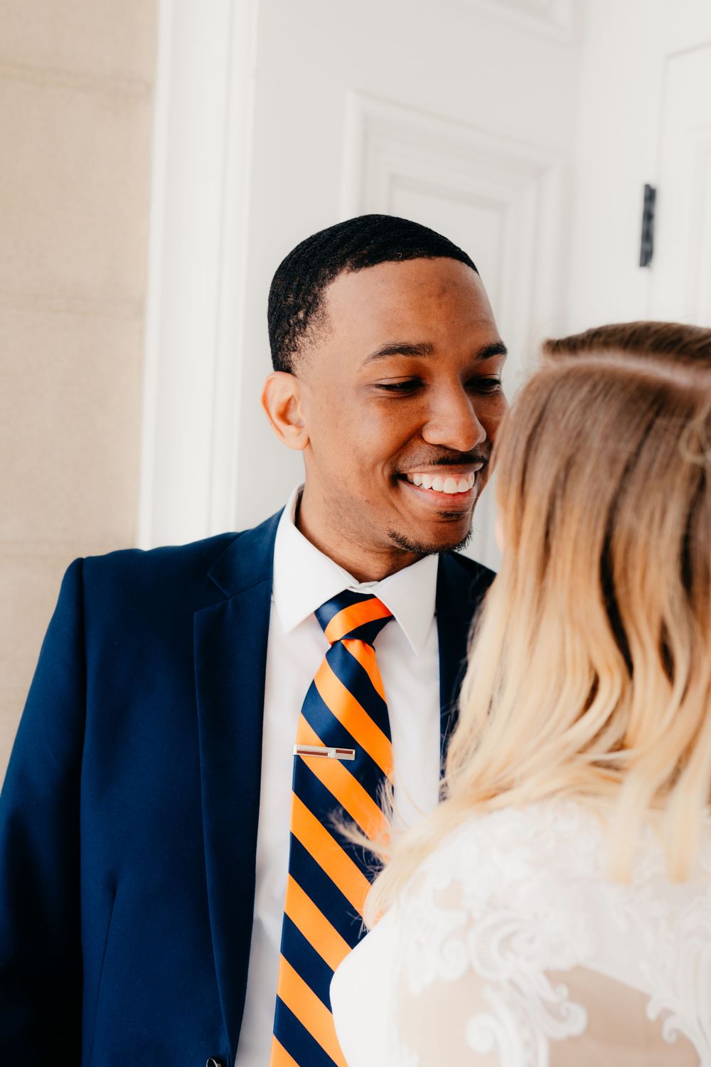 A couple in formal attire shares a tender moment, with the groom wearing a navy suit and orange striped tie.