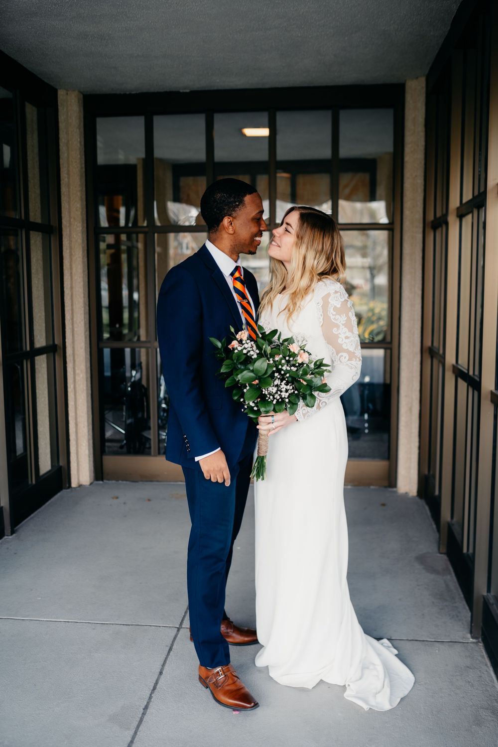 Newlywed couple shares romantic kisses in sequence of photos along a covered walkway with glass windows.