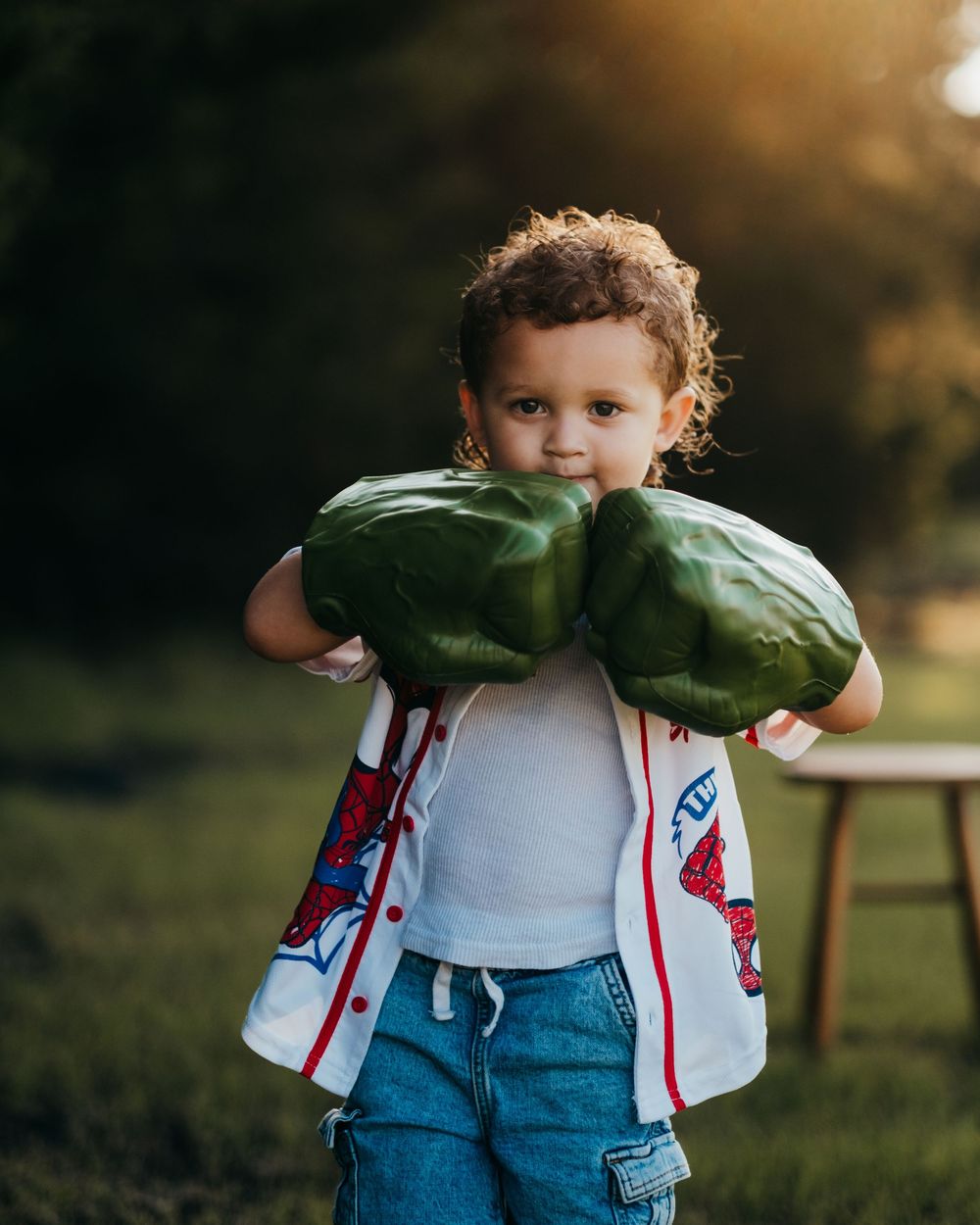 Young boy with curly hair wearing big green Hulk hands and a Spider-Man shirt