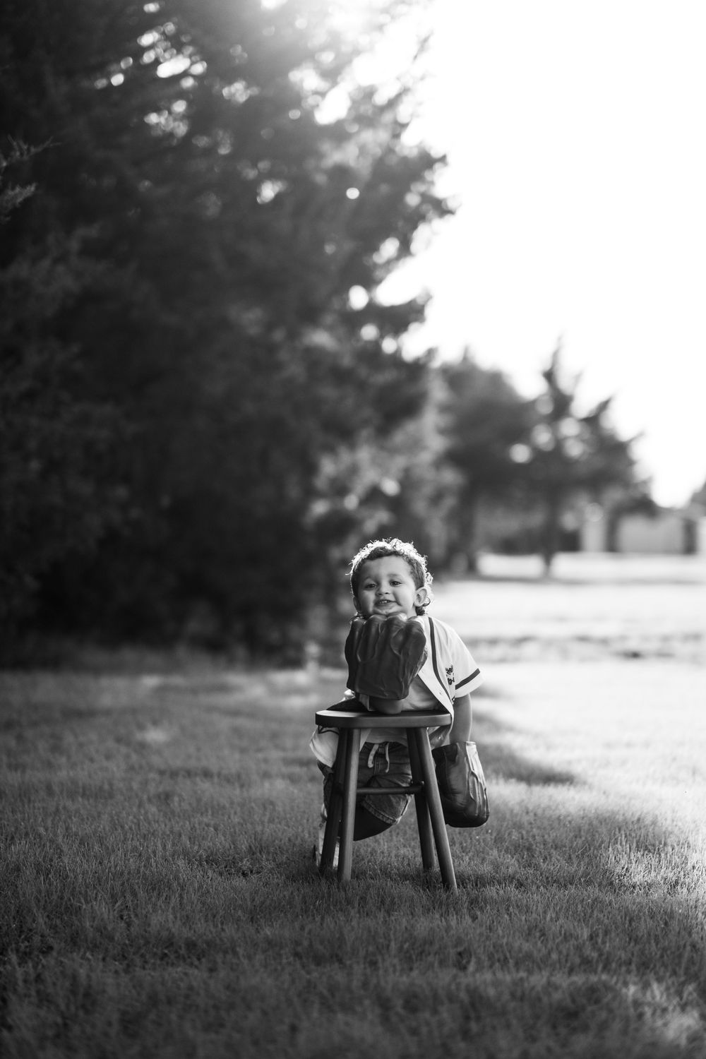 Black and white image of a young boy leaning on a stool in front of trees while wearing Hulk hands