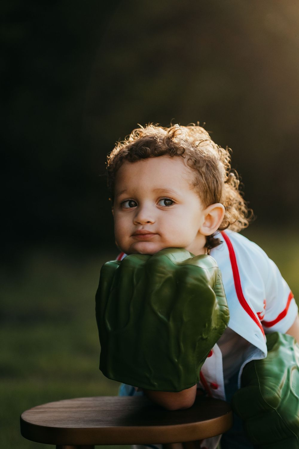 A young boy leans on his giant green Hulk hand and looks away