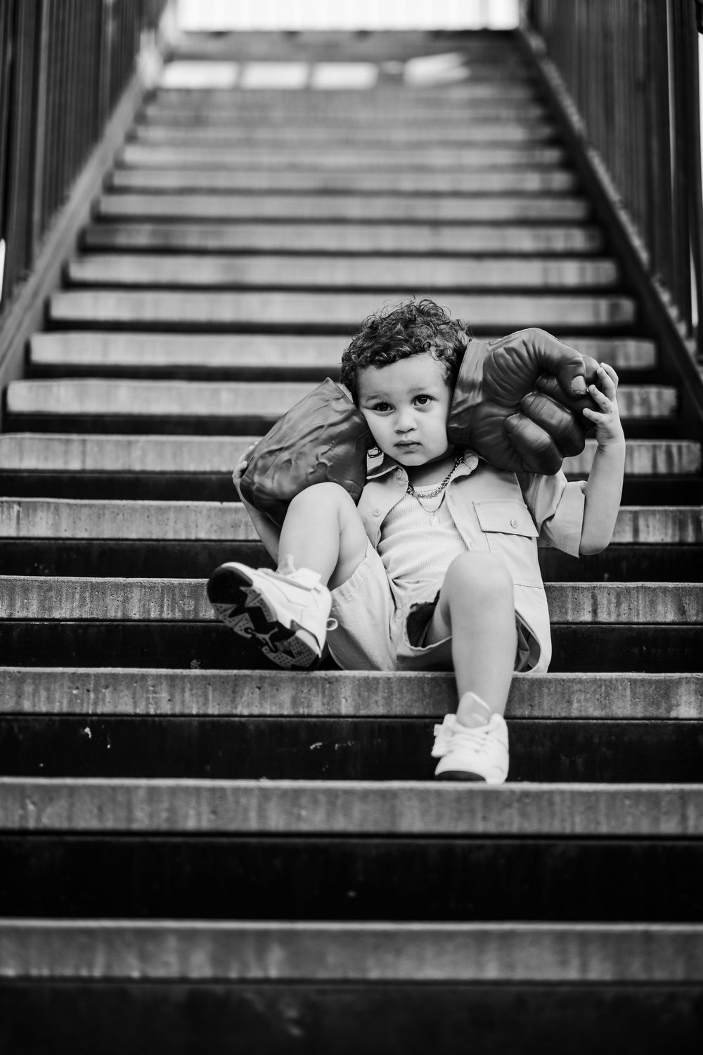 A black and white image of a young boy on the stairs holding Hulk hands up to his cheeks and squishing his face