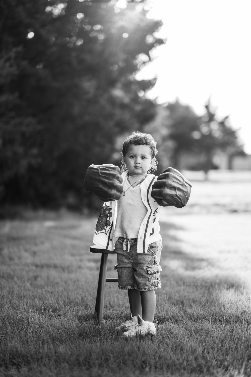 Black and white image of a young boy with curly hair wearing big green Hulk hands while looking at the camera