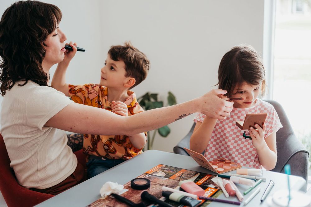 A mother, son, and daughter sit at a table and pretend to do each other's makeup.