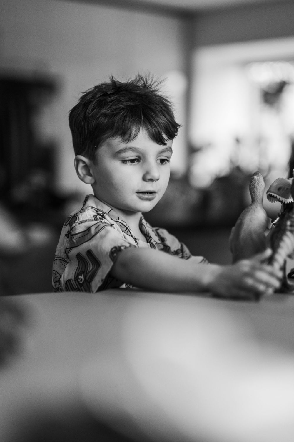 A black and white image of a young boy standing at a table playing with his favorite dinosaur toys