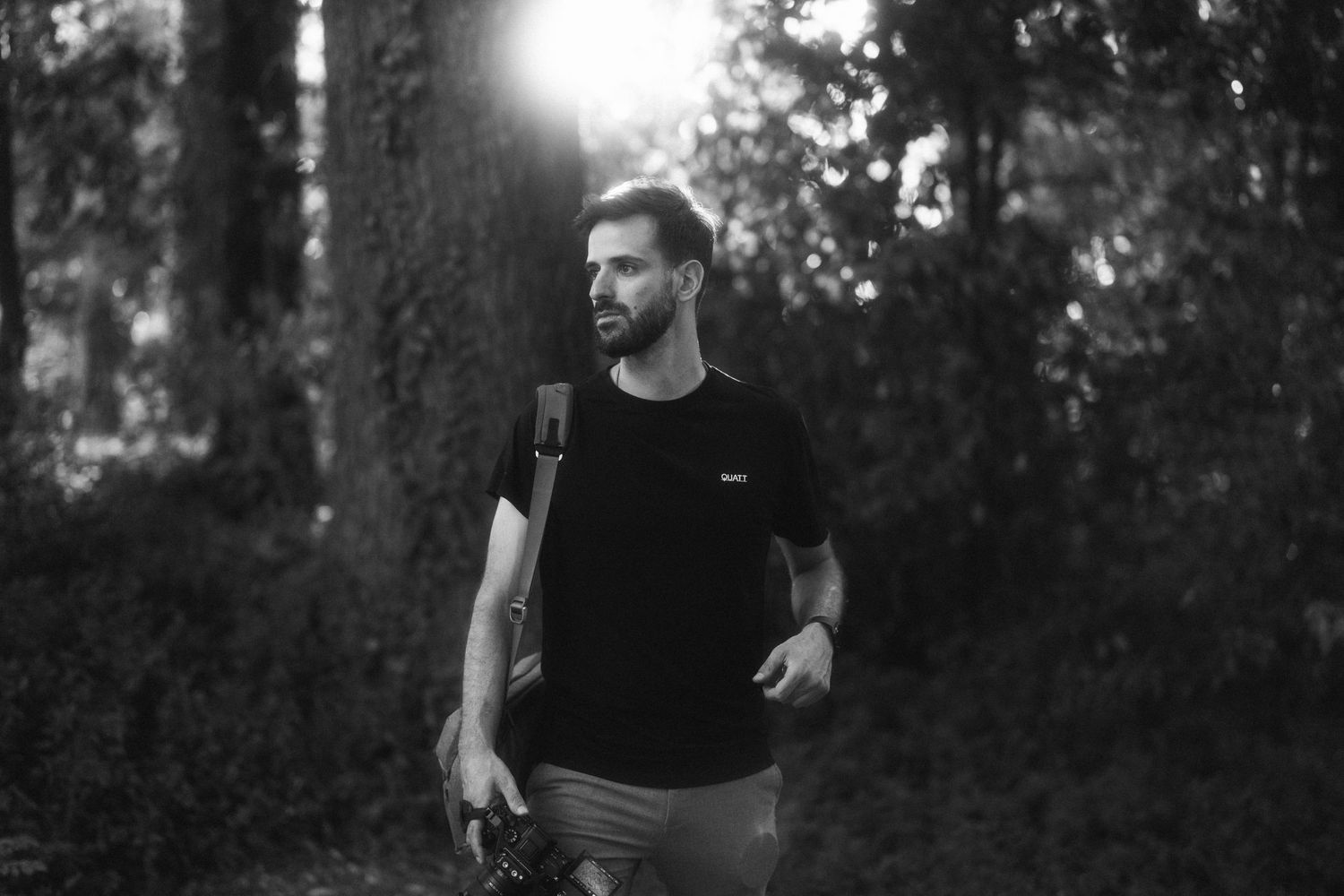 Monochrome photo of a man in casual wear walking through a sunlit forest.