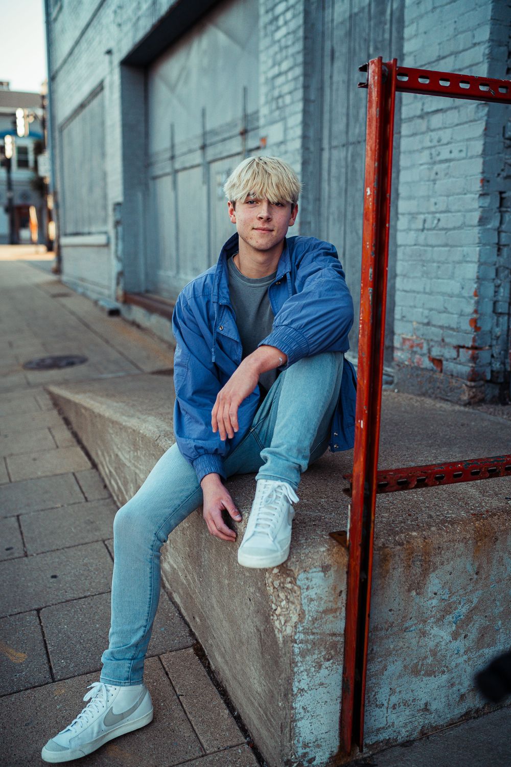 Urban lifestyle portrait against blue brick wall wearing denim jacket and light jeans.
