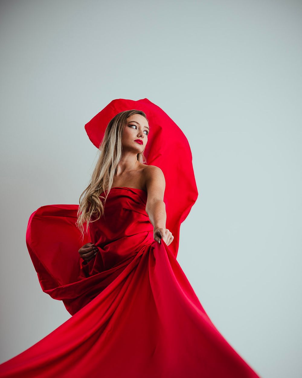 Fashion portrait with model in flowing red gown against light background.