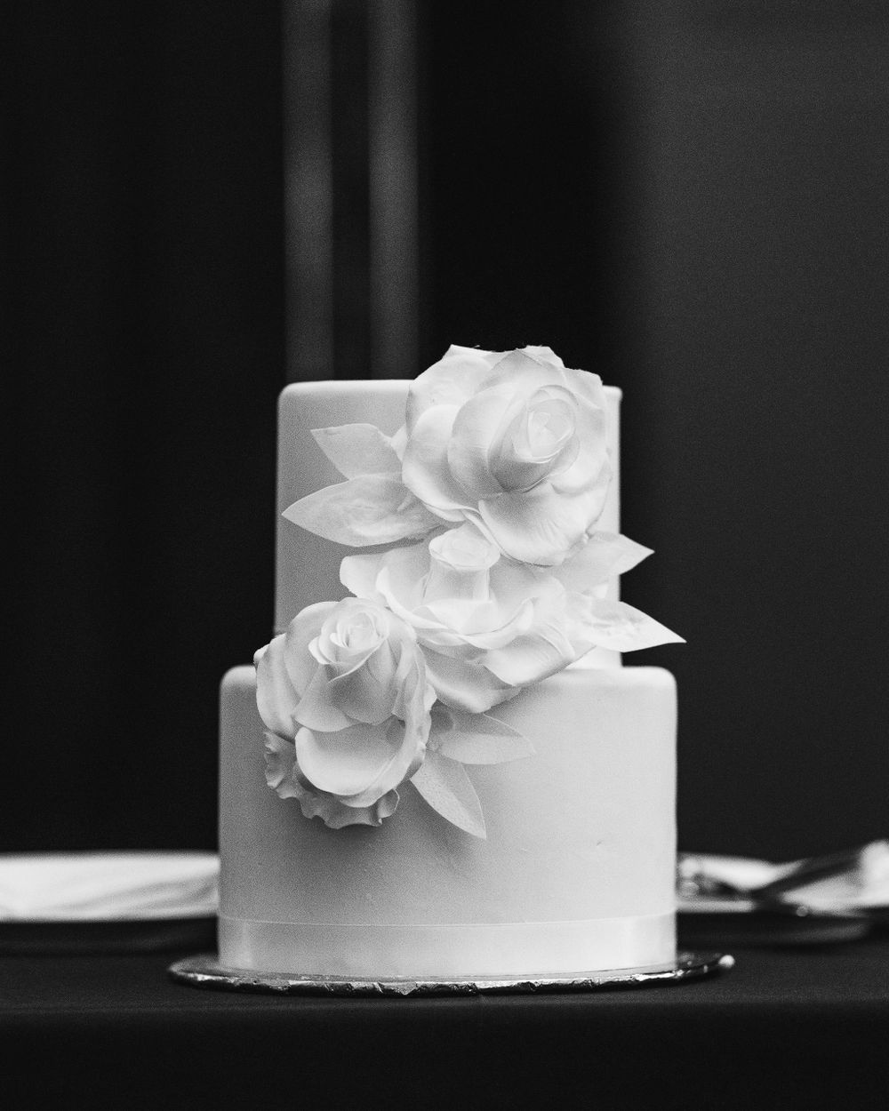 An elegant two-tier white wedding cake decorated with handcrafted sugar roses.