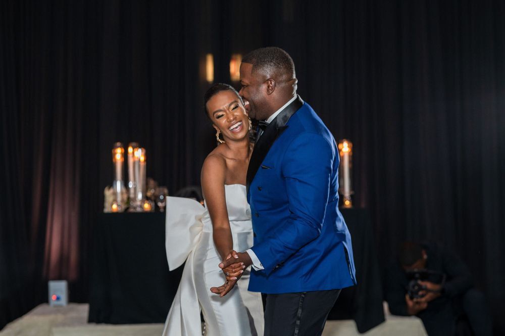 A couple shares their first dance in a dimly lit reception space with candlelight.