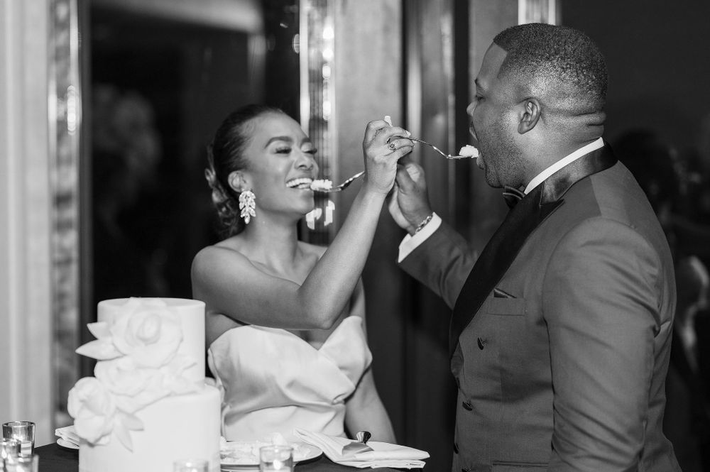 A couple shares a playful moment while feeding each other wedding cake.