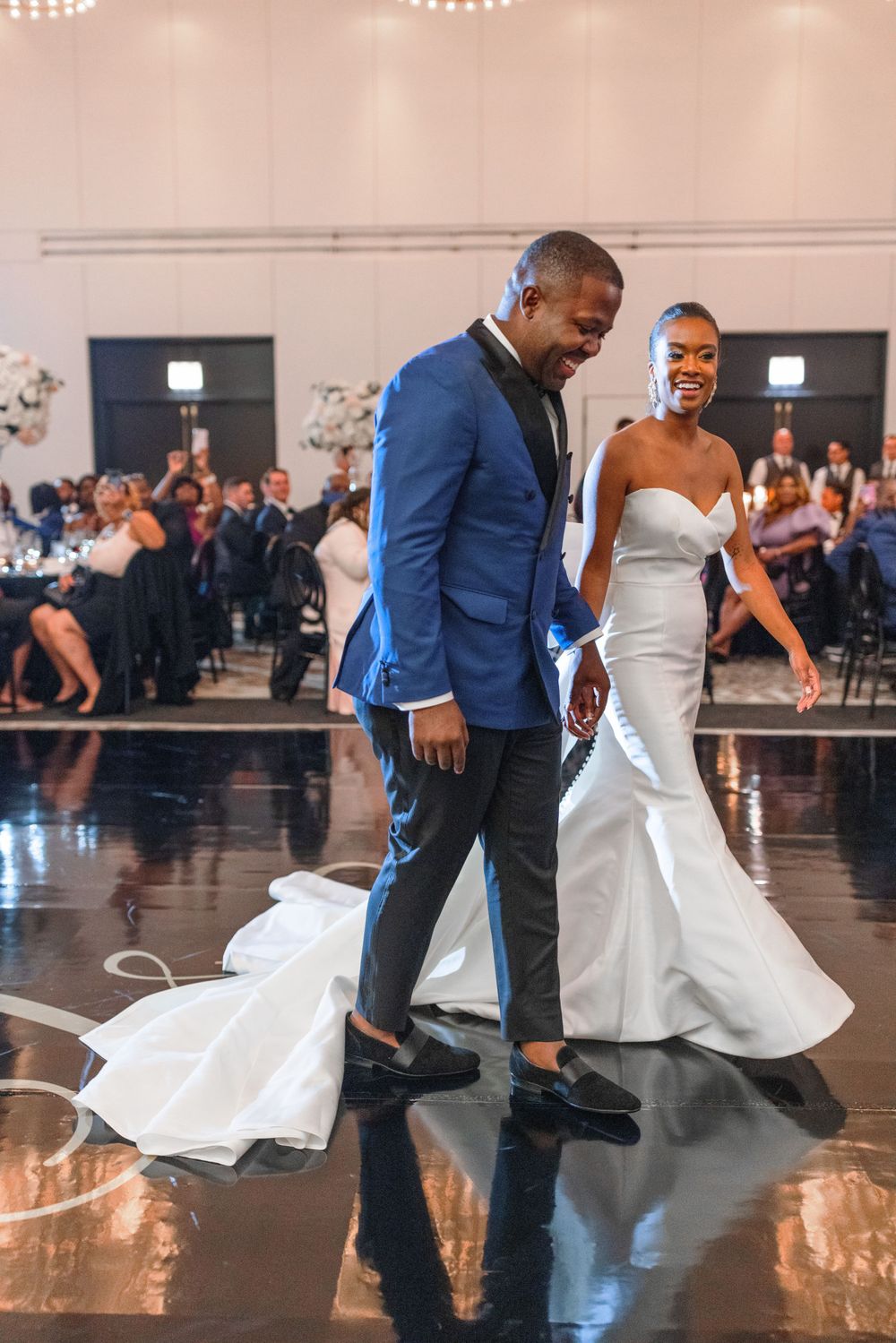 Newlyweds share first dance on reflective floor at indoor wedding reception venue.