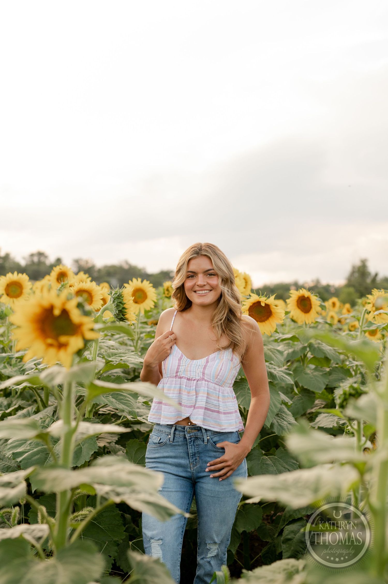 A summer fashion portrait in a vibrant sunflower field with casual denim and crop top styling.