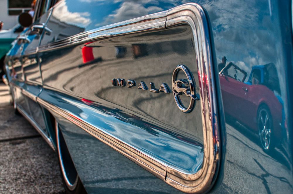 Close-up detail shot of vintage Impala chrome trim and emblem reflecting sunlight.