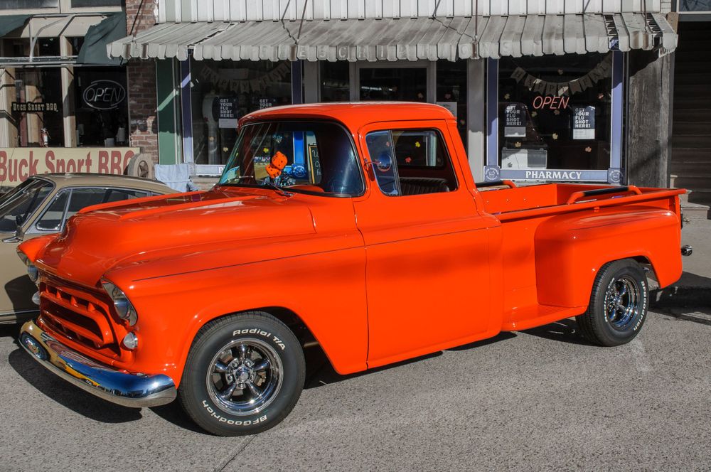 Bright orange vintage Chevrolet pickup truck parked on street with classic styling.