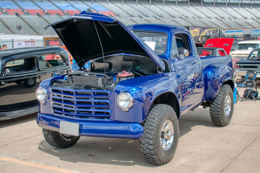 Modified blue Studebaker pickup truck with lifted suspension and oversized tires at car show.