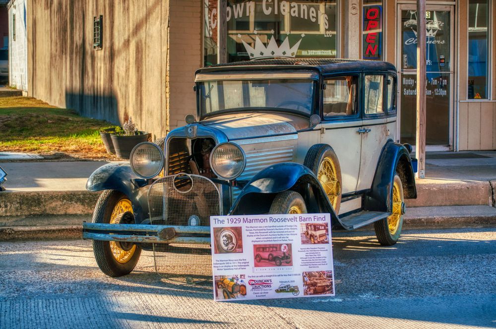 Vintage classic cars displayed in front of a brick building with informational placards.