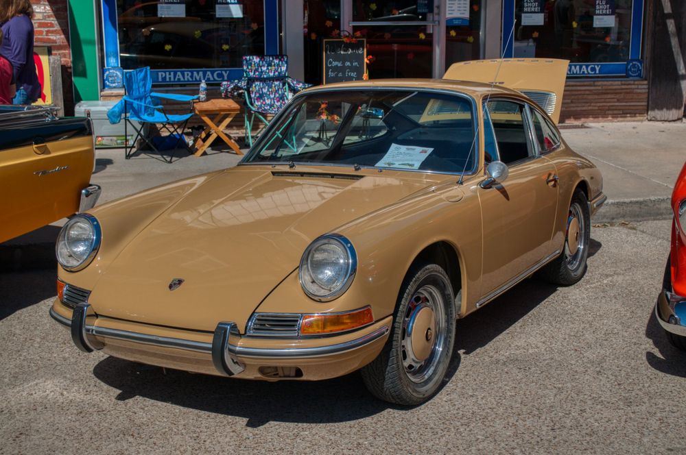 Row of tan and gold colored Porsche 911 classic sports cars on display.