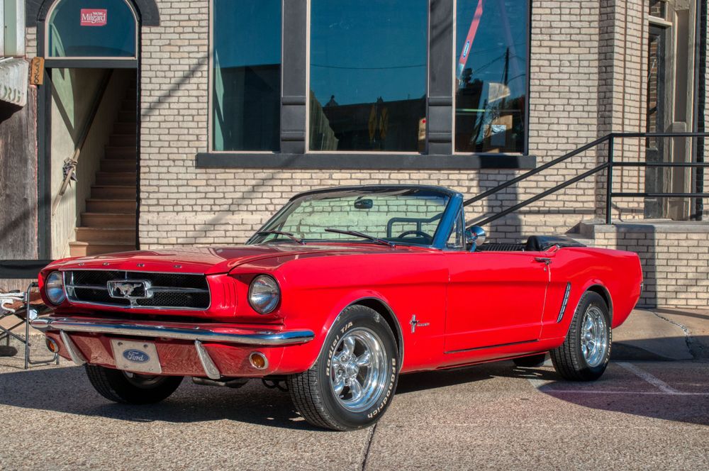 Multiple bright red classic muscle cars lined up at an outdoor car show.