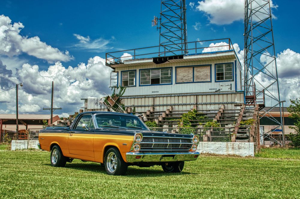 Classic orange Ford car parked in front of a vintage control tower structure.