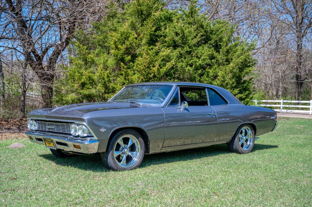 Classic grey Chevrolet Chevelle muscle car parked on green lawn near trees.