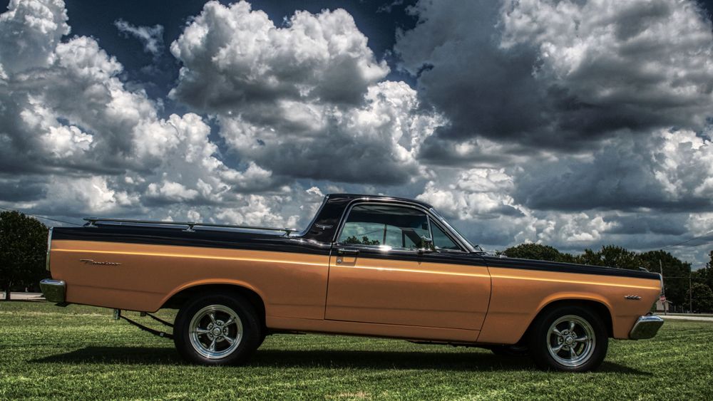 Vintage copper-colored classic car photographed against dramatic cloudy sky.