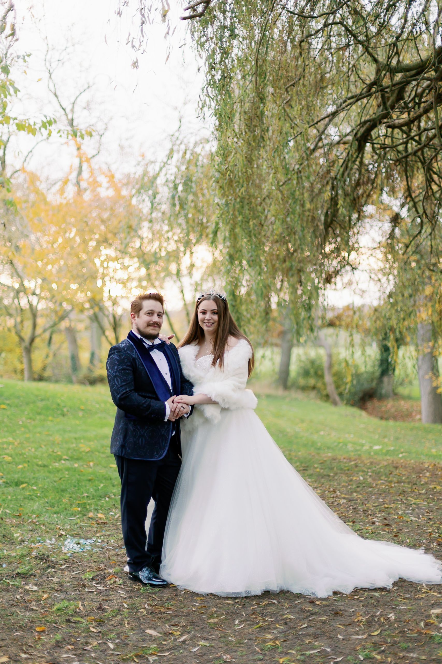 Happy couple poses for wedding portrait under weeping willow trees in autumn. Essex Wedding Photographer