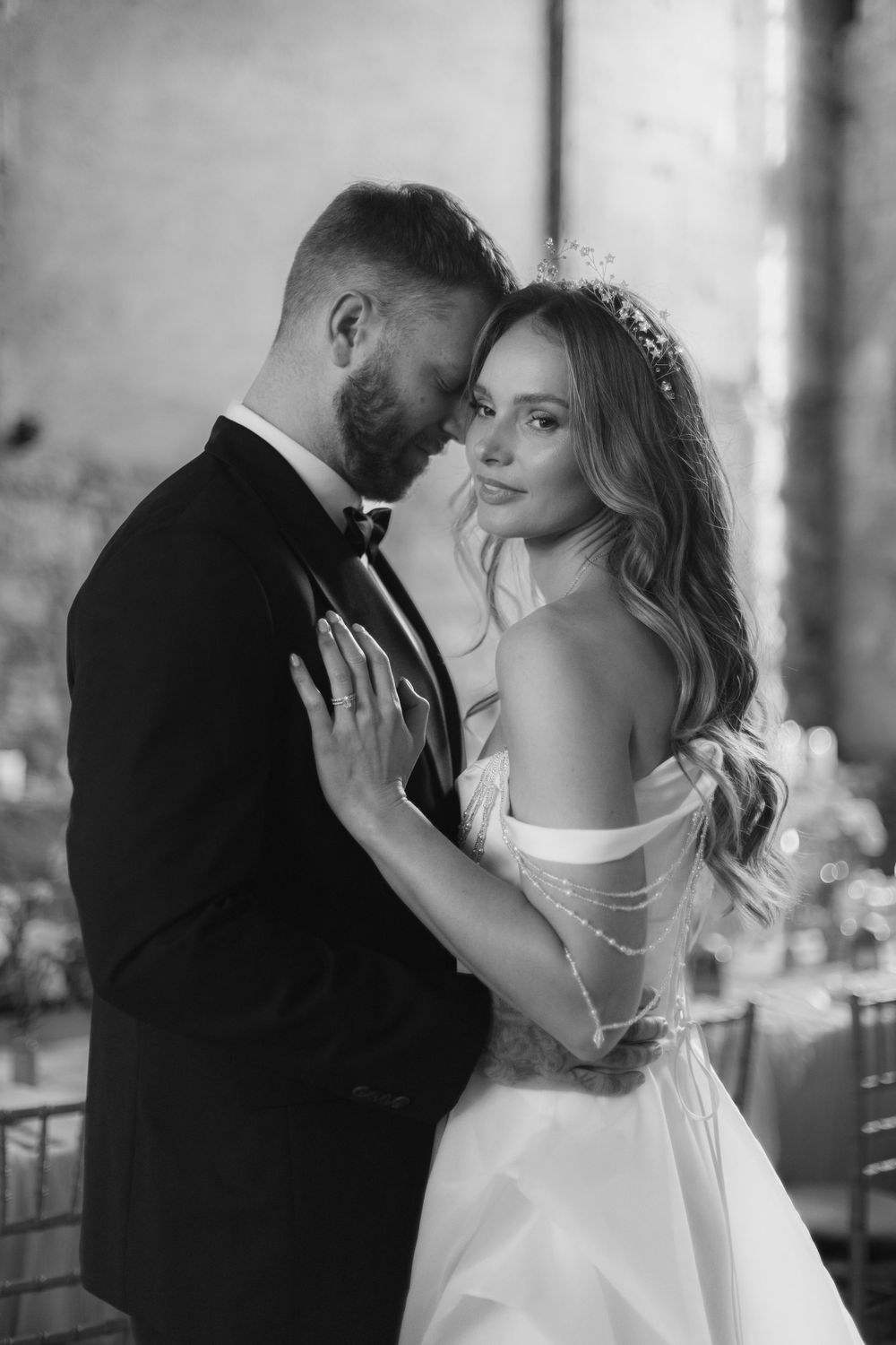 Black and white romantic wedding photo of newlyweds embracing in an intimate moment wearing formal attire.