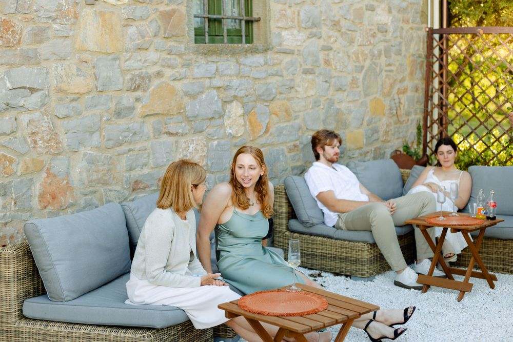 Guests relaxing on outdoor patio furniture at a stone villa during a social gathering.