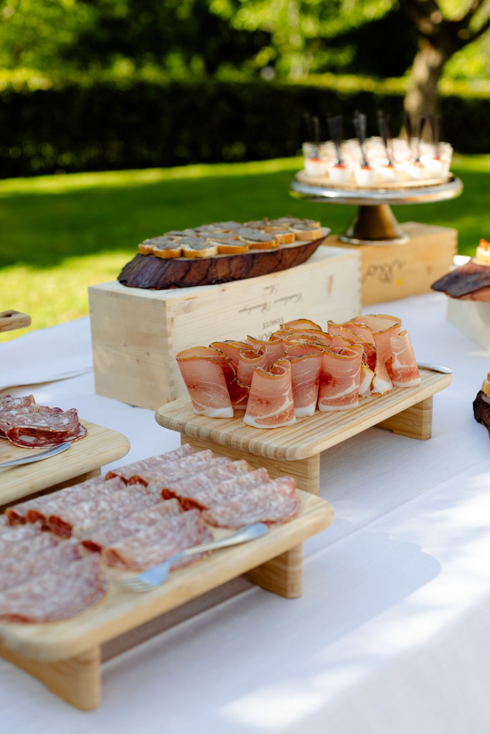 Elegant food display with appetizers and desserts arranged on wooden platforms at an outdoor event.