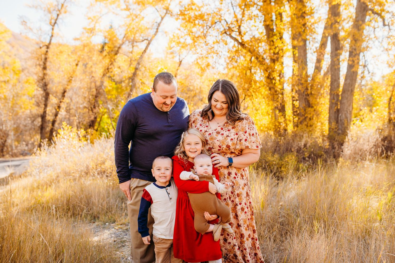 Family enjoying autumn weather together in field with golden trees in background.