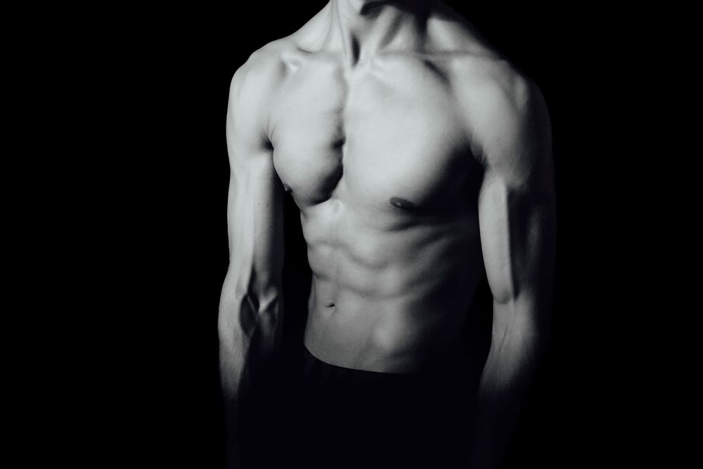 Monochromatic portrait study focusing on male torso against dark background.