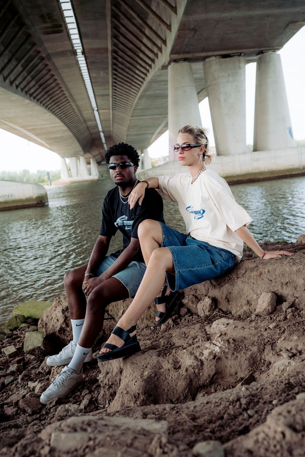 People relaxing under a bridge near water on a sunny day.