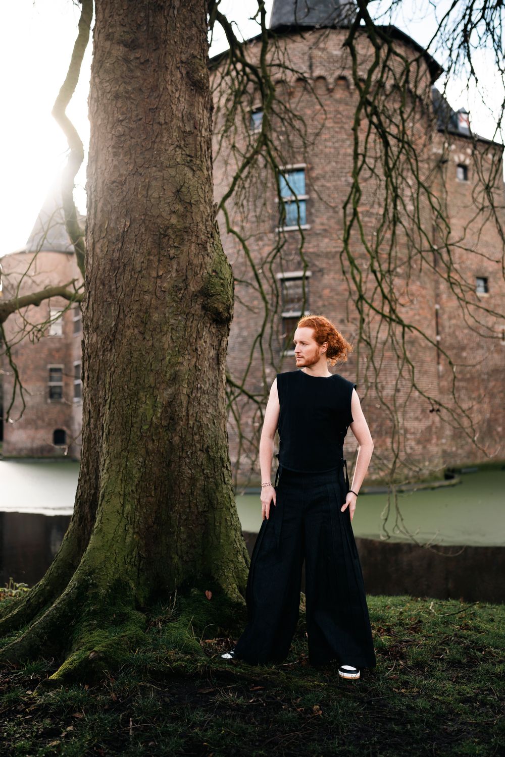 A series of artistic photos showing a person in a black dress posed against a large tree trunk with brick buildings in background.
