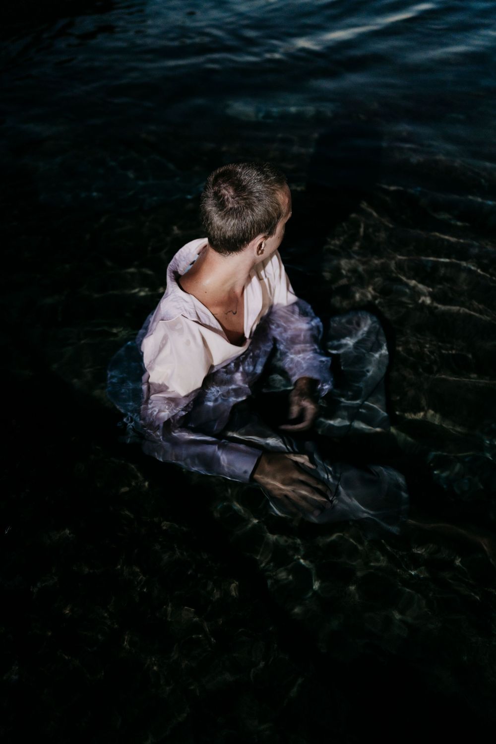 A figure submerged in dark water wearing white fabric creates a dramatic and ethereal underwater scene.