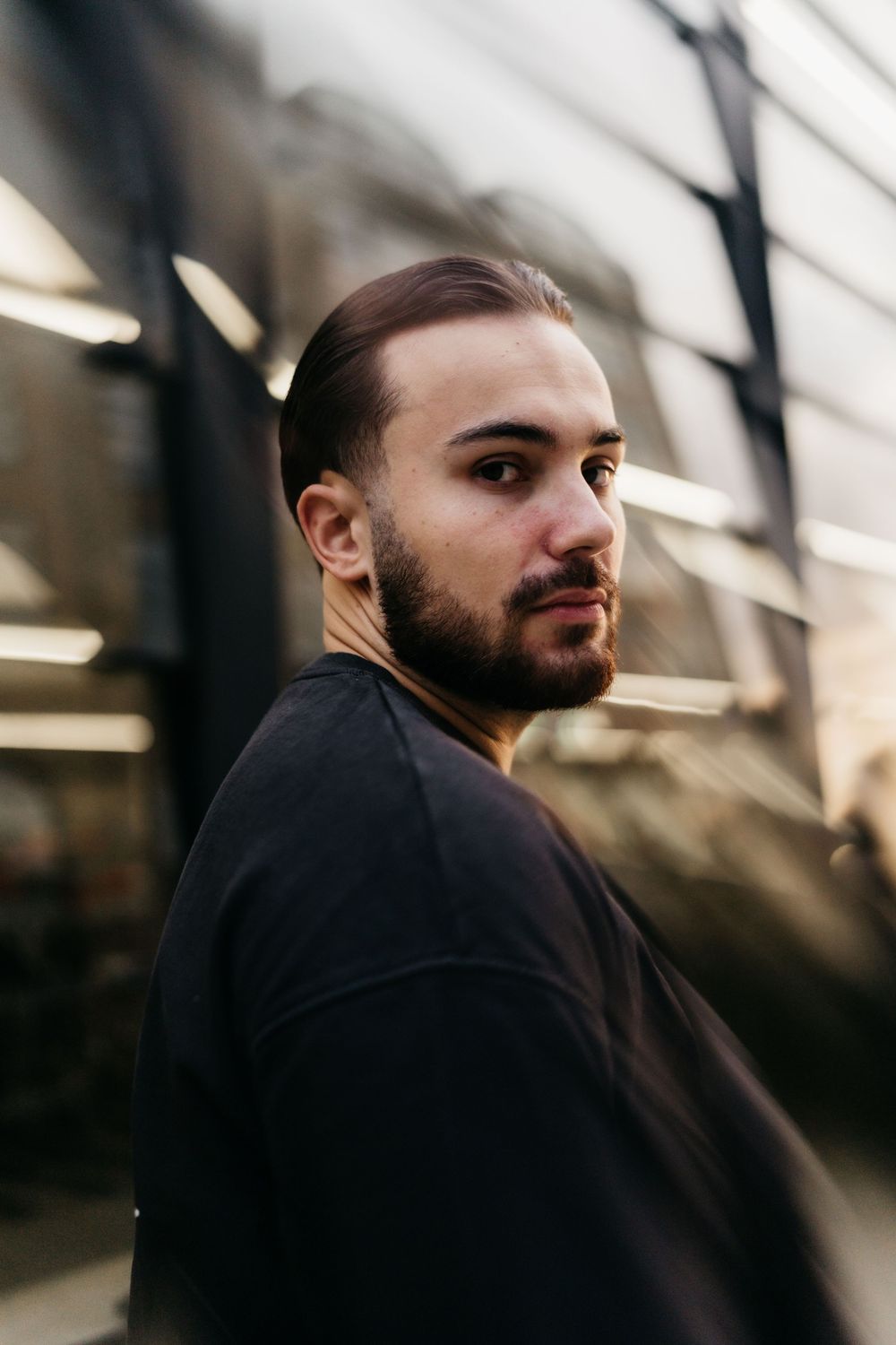 Portrait of a person with a beard wearing a black sweater in moody outdoor lighting with blurred background.