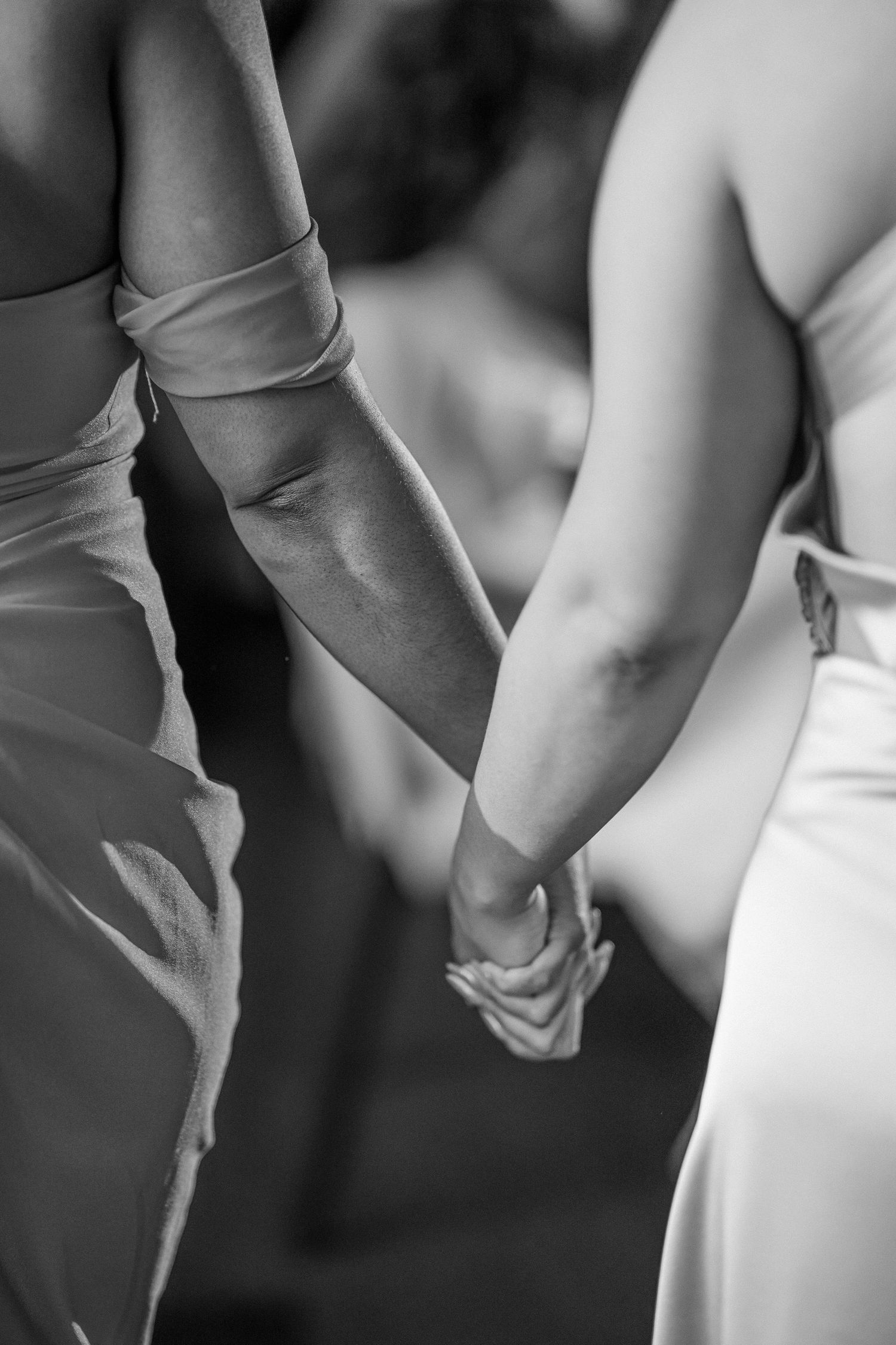Close-up black and white shot of a couple holding hands in formal wedding attire.