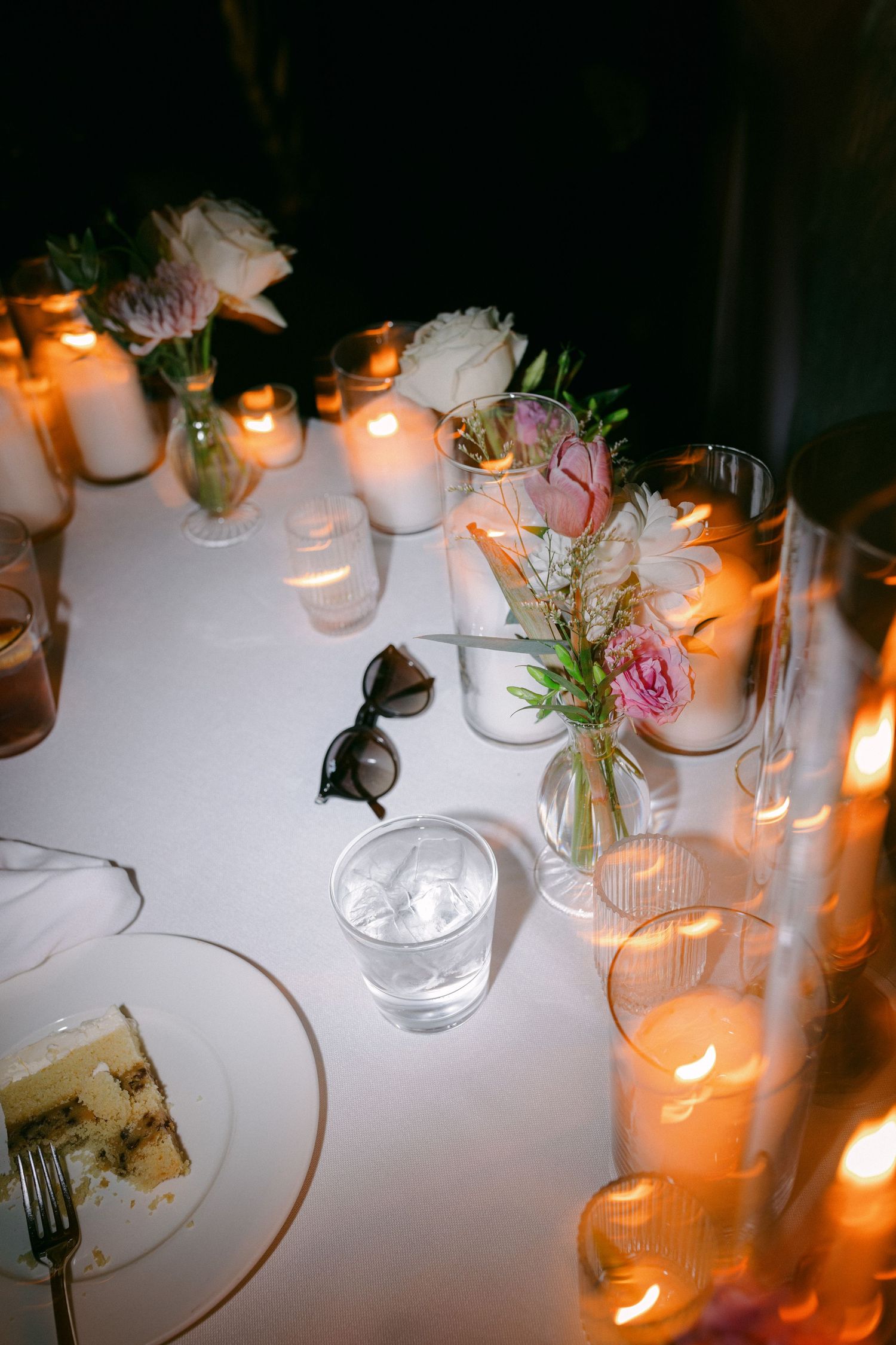 Wedding reception table with lit candles, delicate flower arrangements, and place settings.
