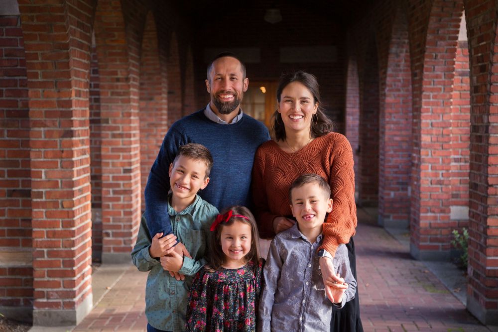 A family of five stands together in a covered brick walkway on a sunny day.