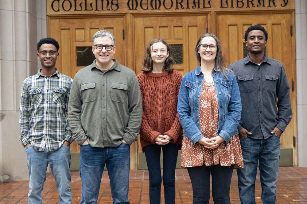 A group of students stands together smiling in front of Collins Memorial Library entrance.