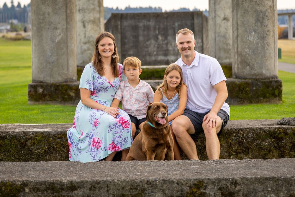 A family and their dog pose together for outdoor portraits on stone steps in a park setting.