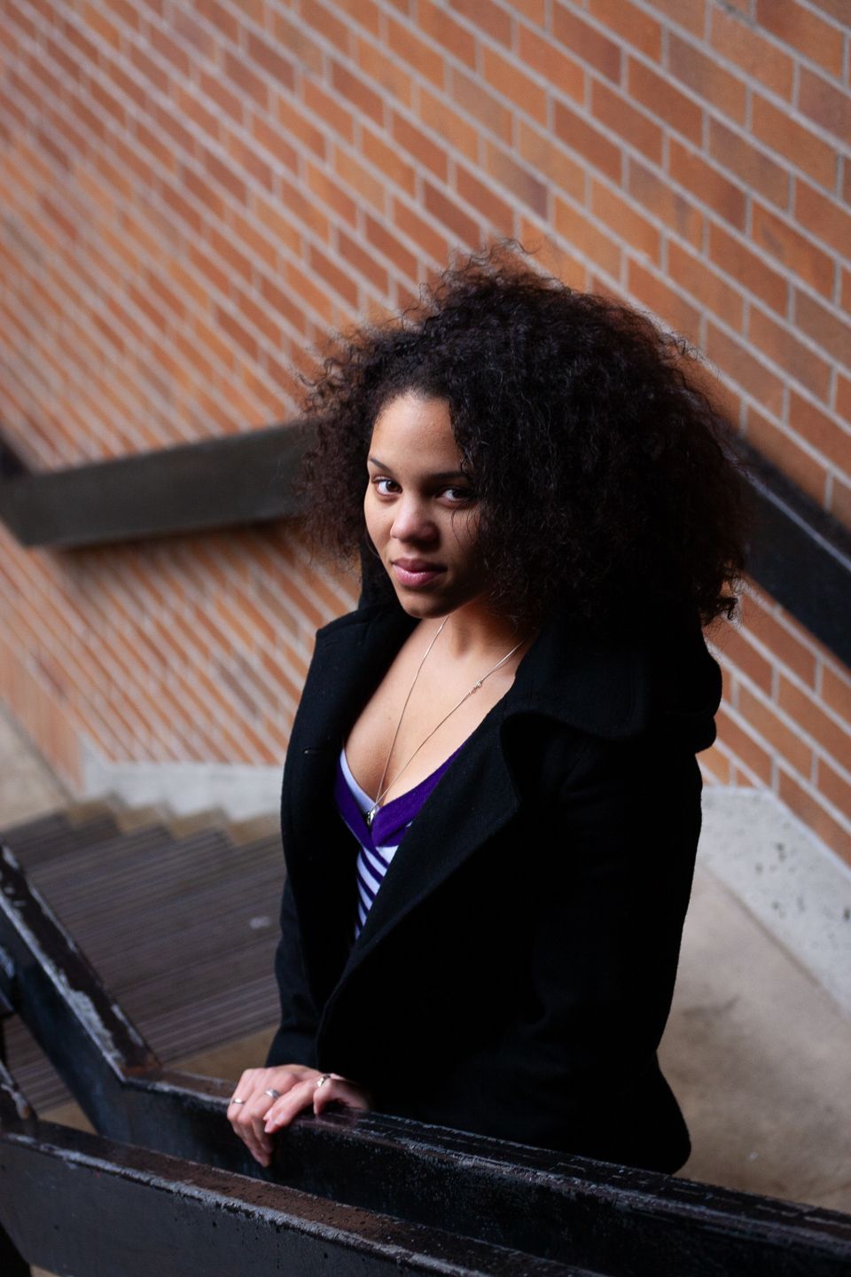 Portrait on staircase wearing black blazer against brick wall background.