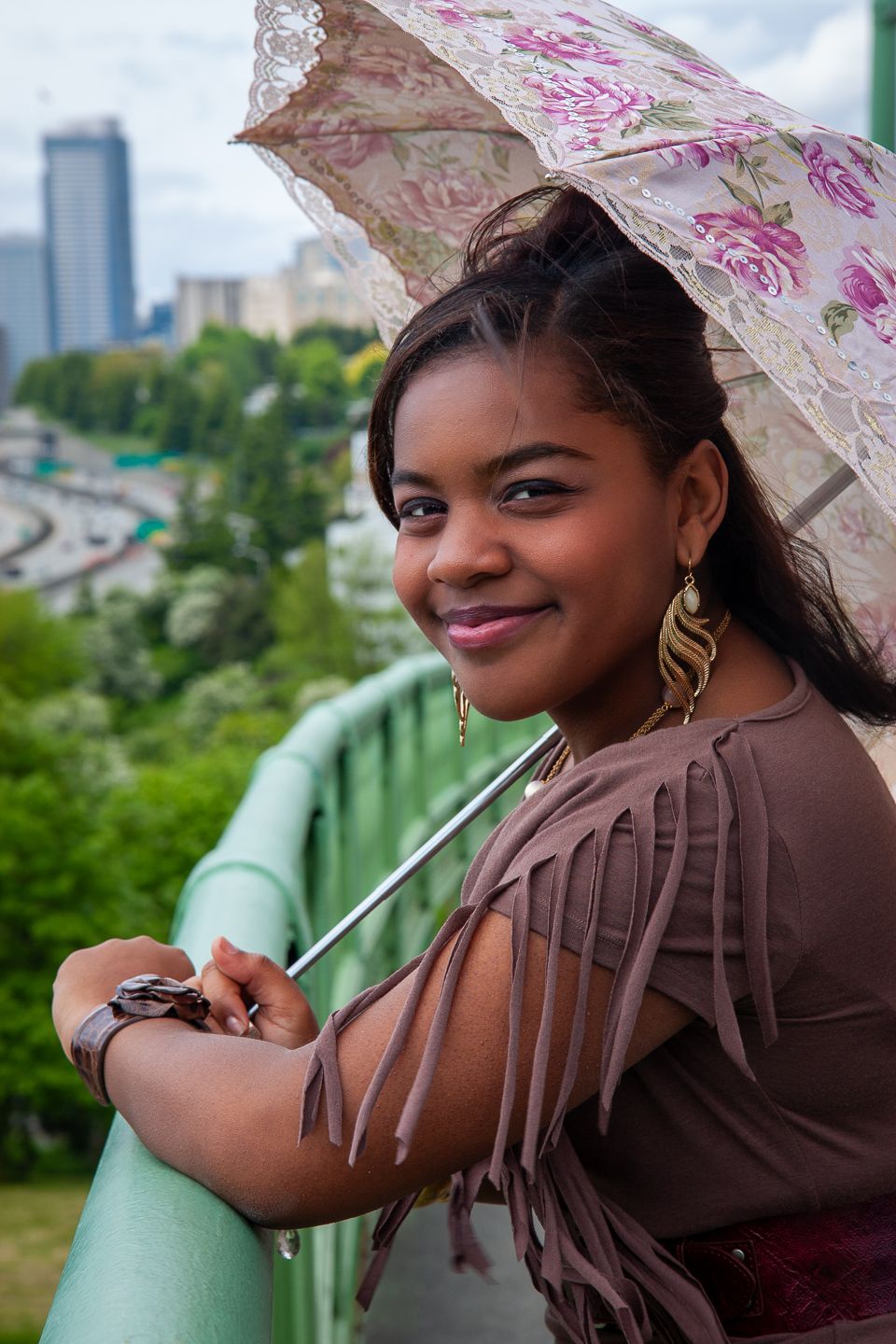 Portrait with floral umbrella overlooking city skyline on green railing.