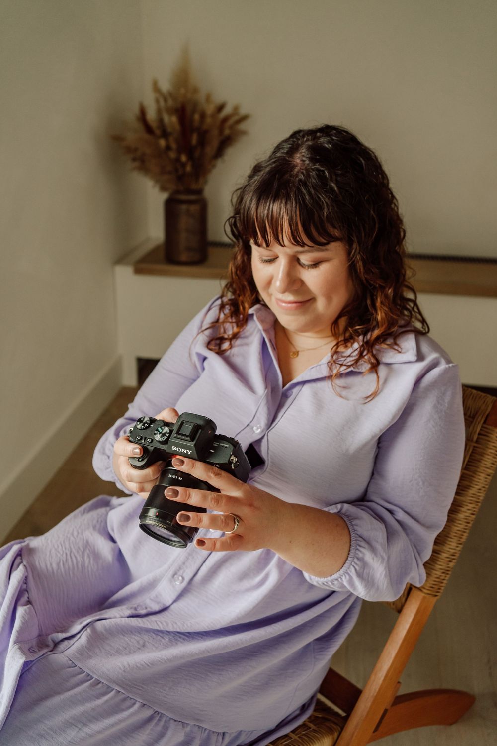 vrouw met lila jurk zittende in rotan stoel met fototoestel in de hand en kijkende naar foto's