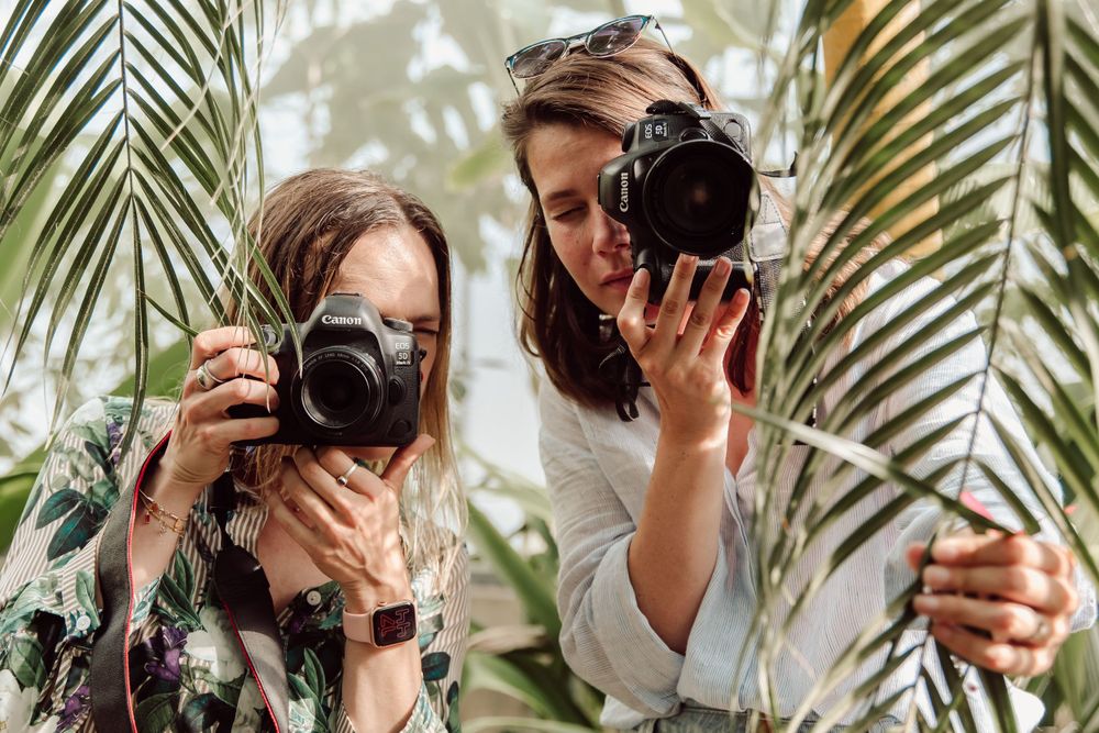 2 vrouwen met fototoestel in de hand die foto nemen tussen de bladeren
