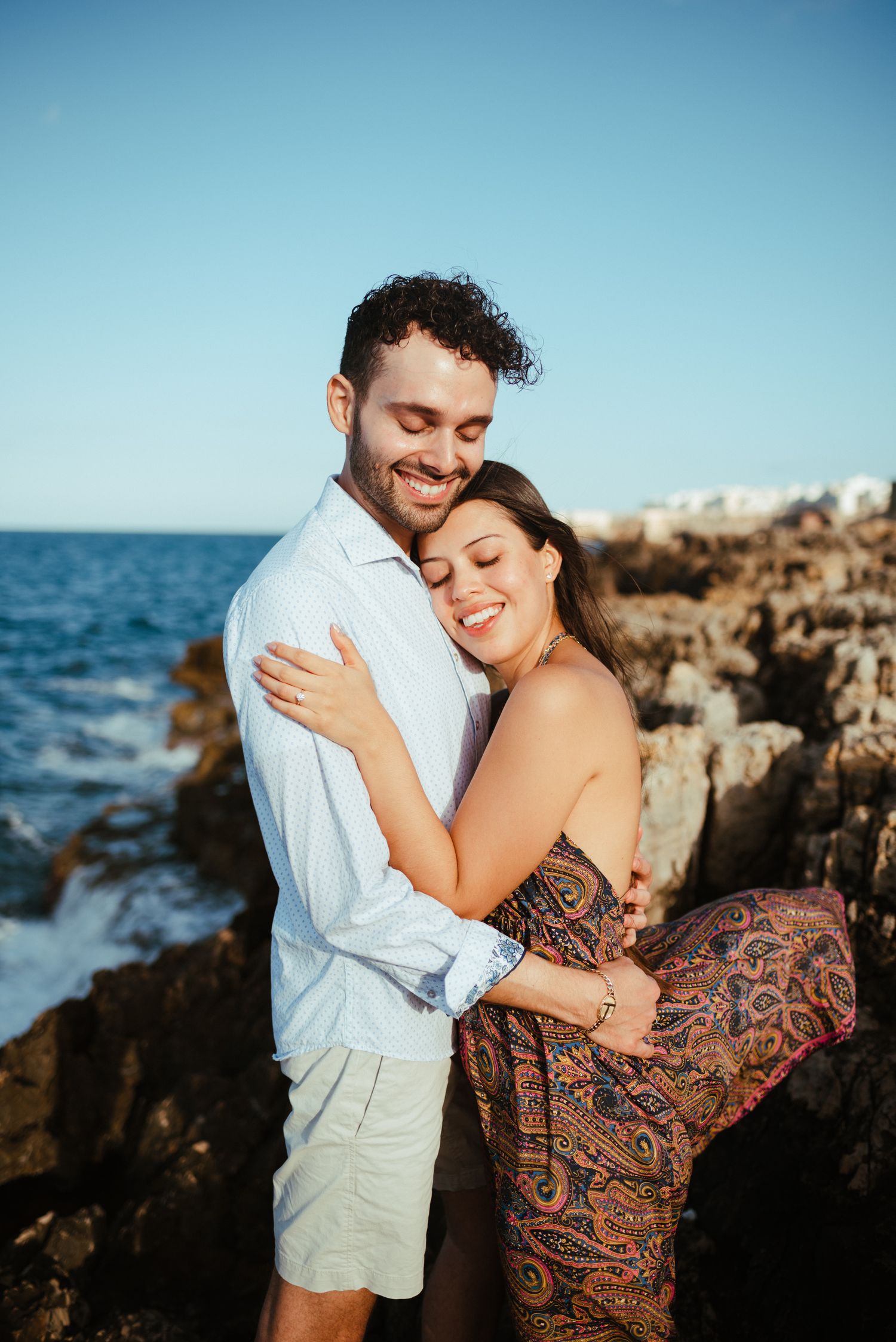 A couple shares an intimate moment on rocky coastal cliffs at sunset.