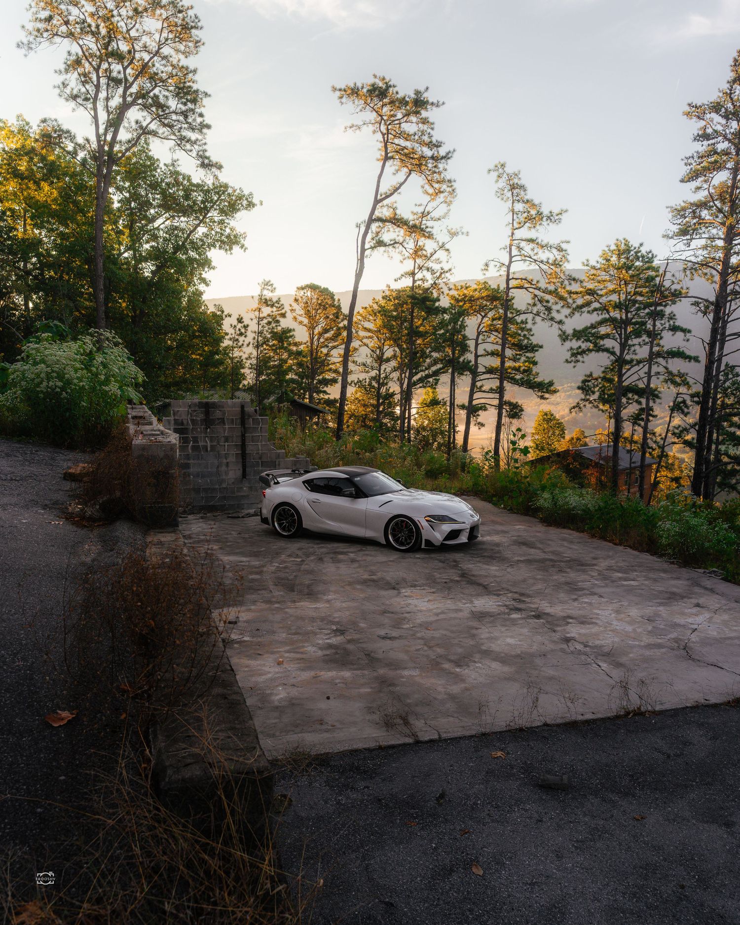 White sports car parked on concrete overlook with scenic forest view at sunset.