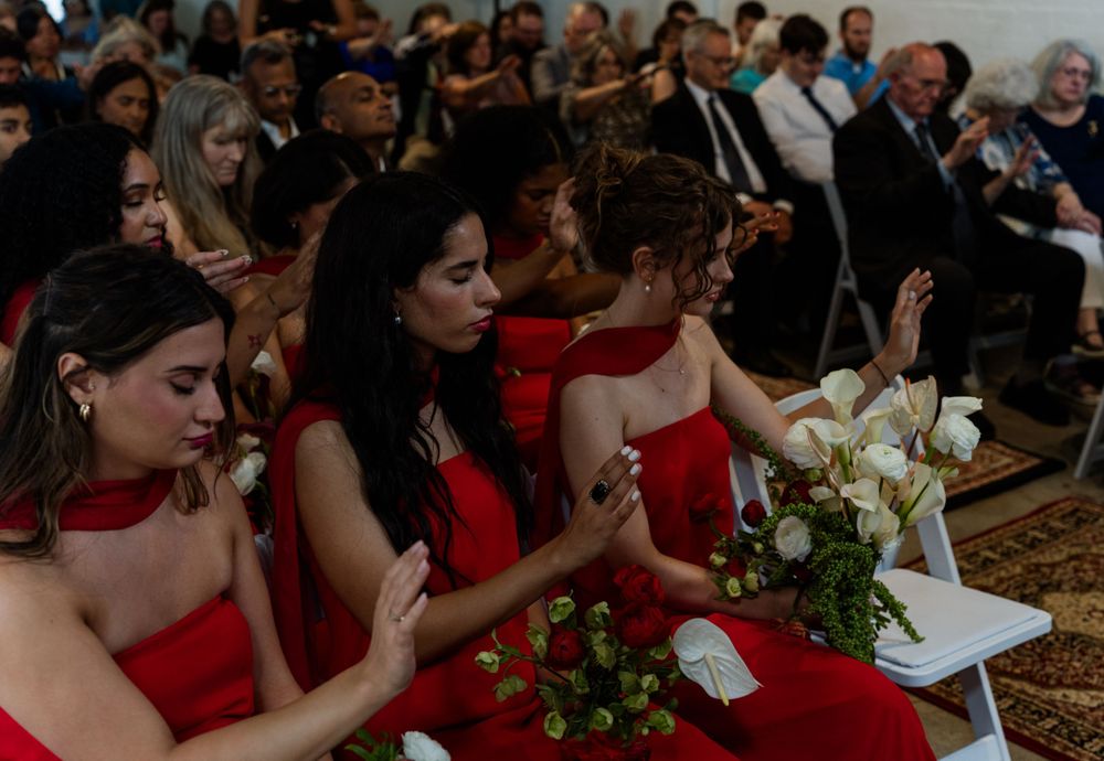 Bridesmaids in red dresses seated at wedding reception with floral centerpieces.