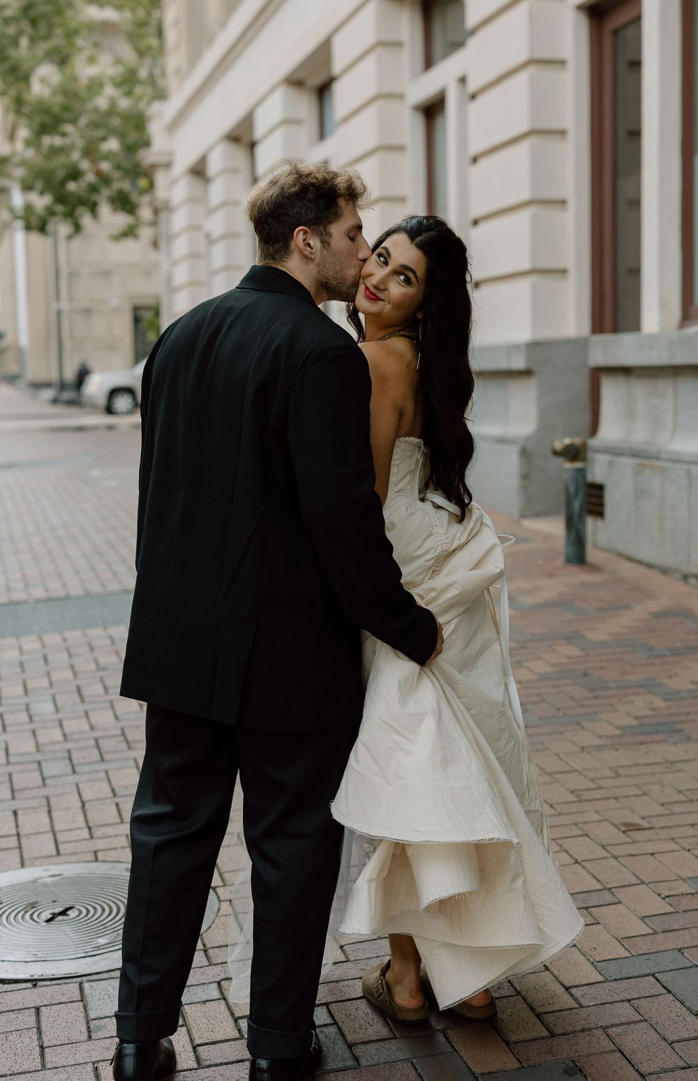Romantic couple in formal wear sharing an intimate moment on a brick sidewalk downtown.