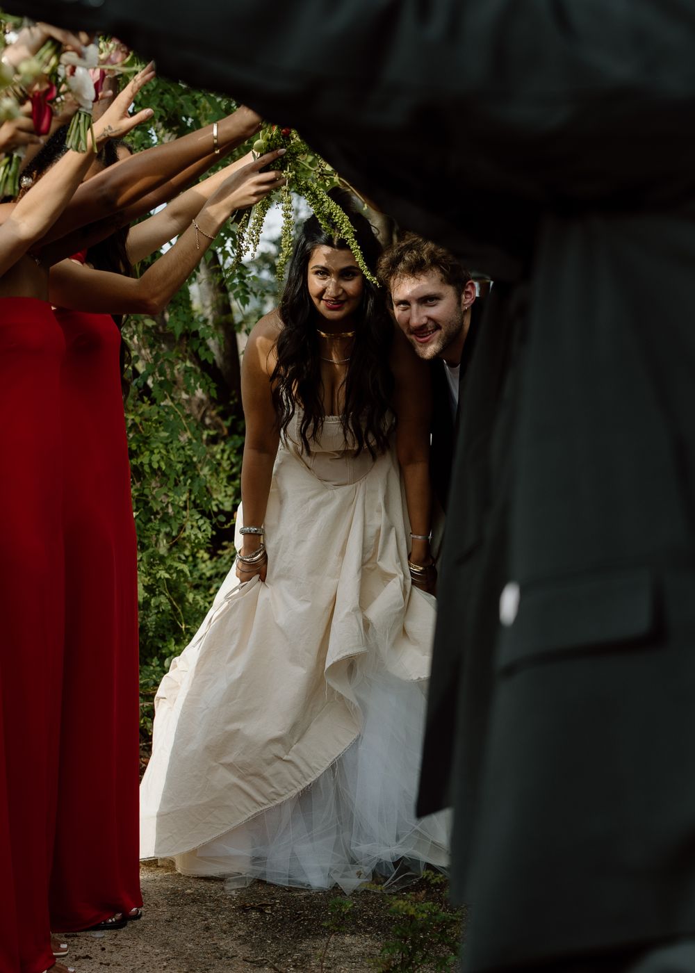 A couple celebrates their wedding day surrounded by guests raising their hands in celebration.
